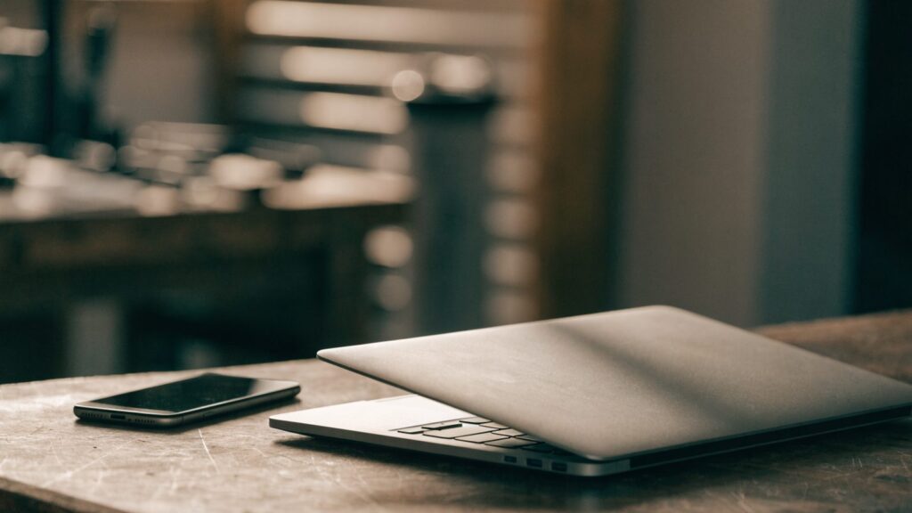 A smartphone lying beside a silver laptop on a workbench