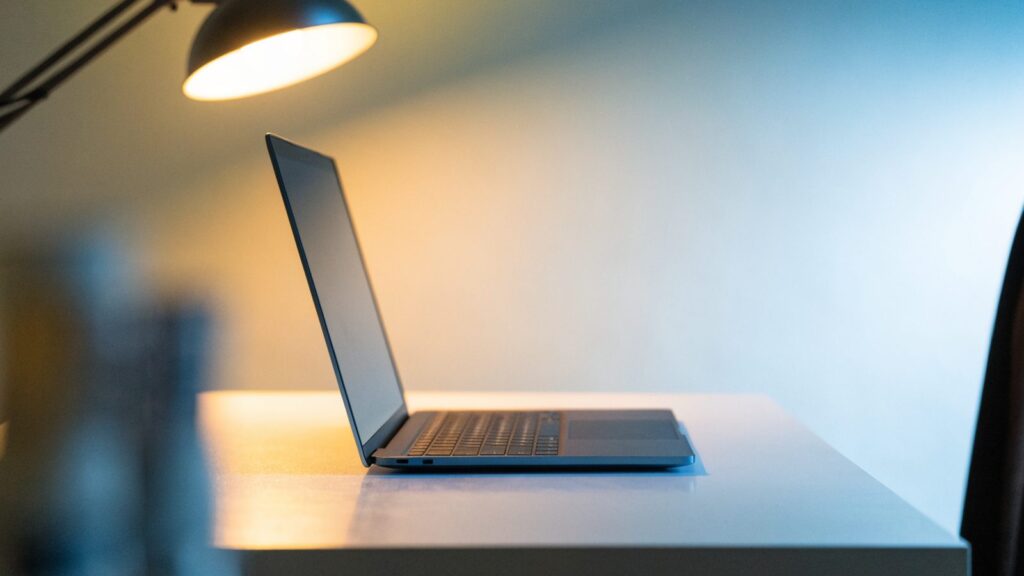 A sleek modern dark blue laptop centered on a white desk against a clean soft gradient background