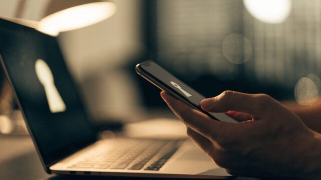 A hand holding a smartphone beside a silver laptop
