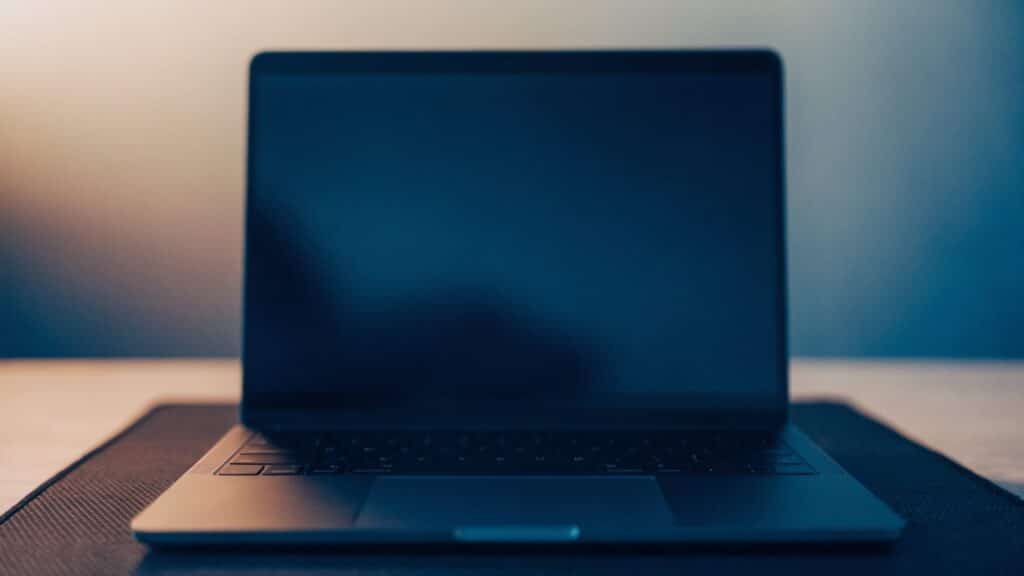 A sleek modern dark blue laptop centered on a dark desk mat against a clean soft gradient background
