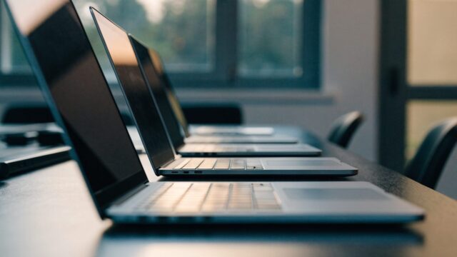 Several modern laptops lined up in a row on an office desk