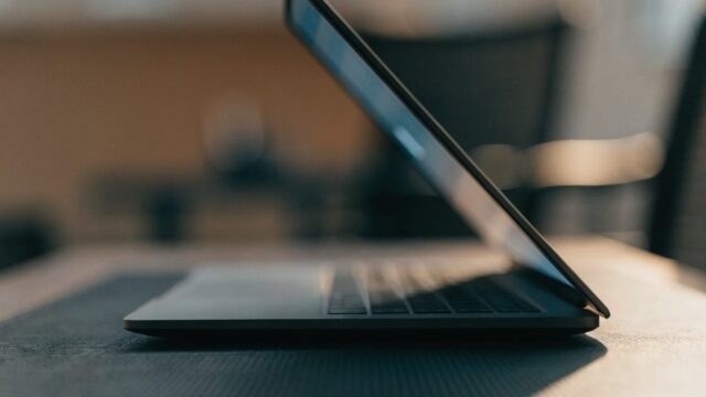 A graphite laptop half open on a dark desk, its screen glow spilling onto the desk