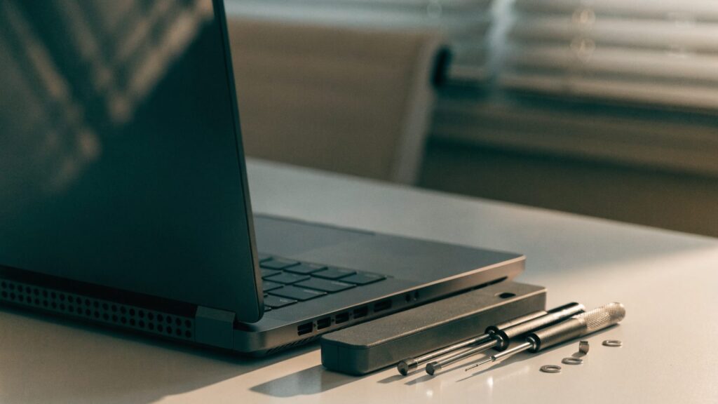A precision screwdriver kit laid out beside a partially opened graphite black laptop on a white desk