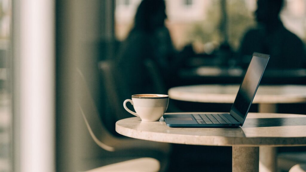 A dark blue laptop open on a cafe table beside a cup of coffee