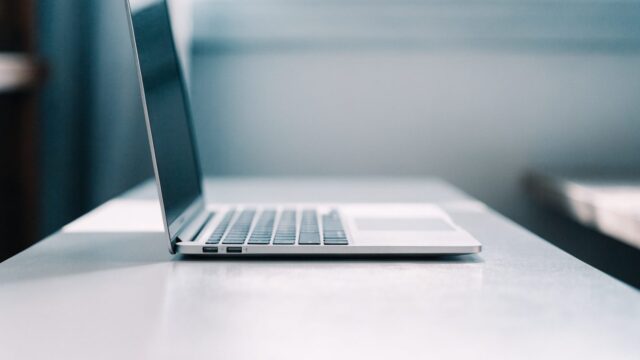 A sleek modern silver laptop centered on a white desk against a clean soft gradient background