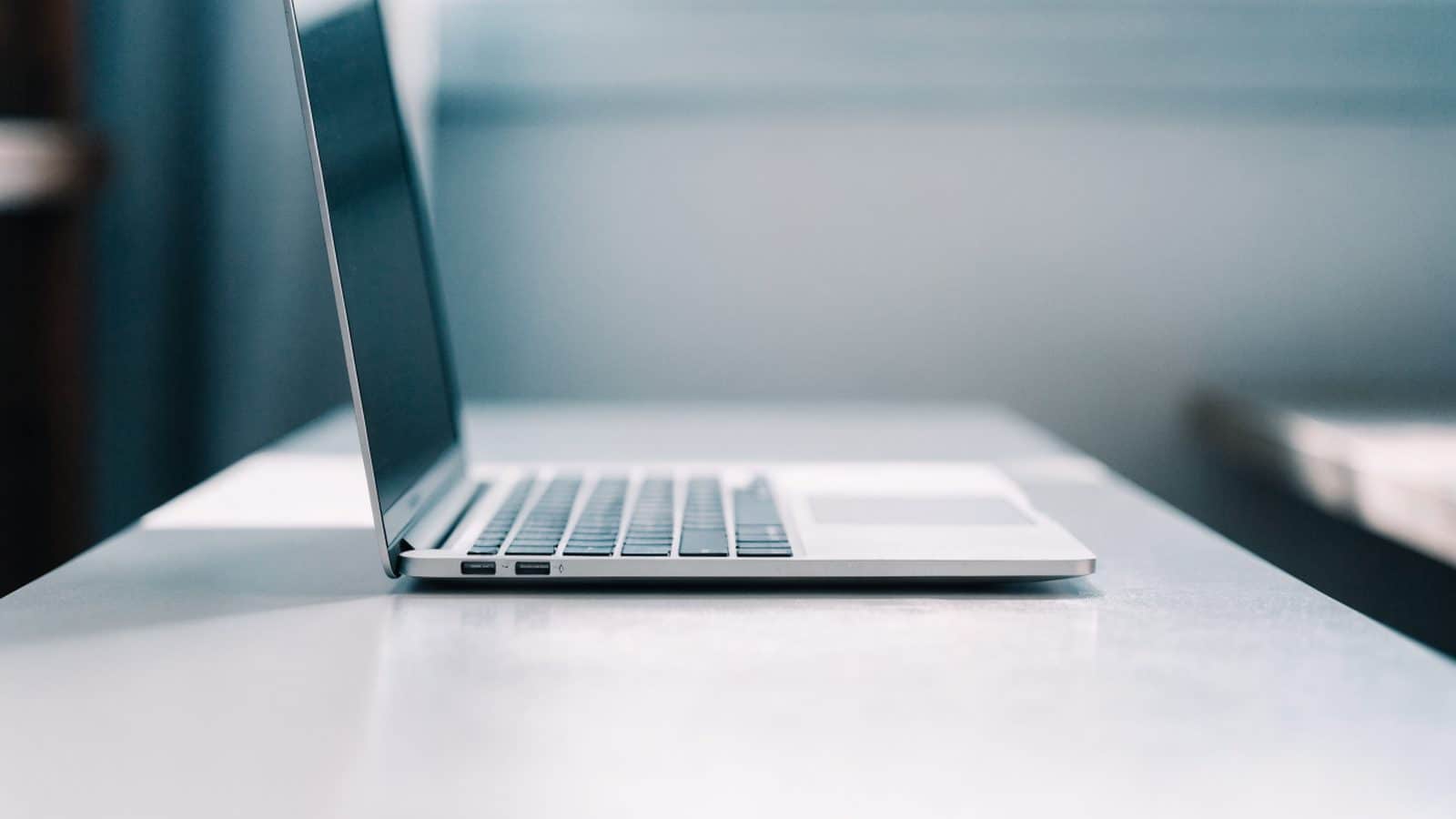 A sleek modern silver laptop centered on a white desk against a clean soft gradient background