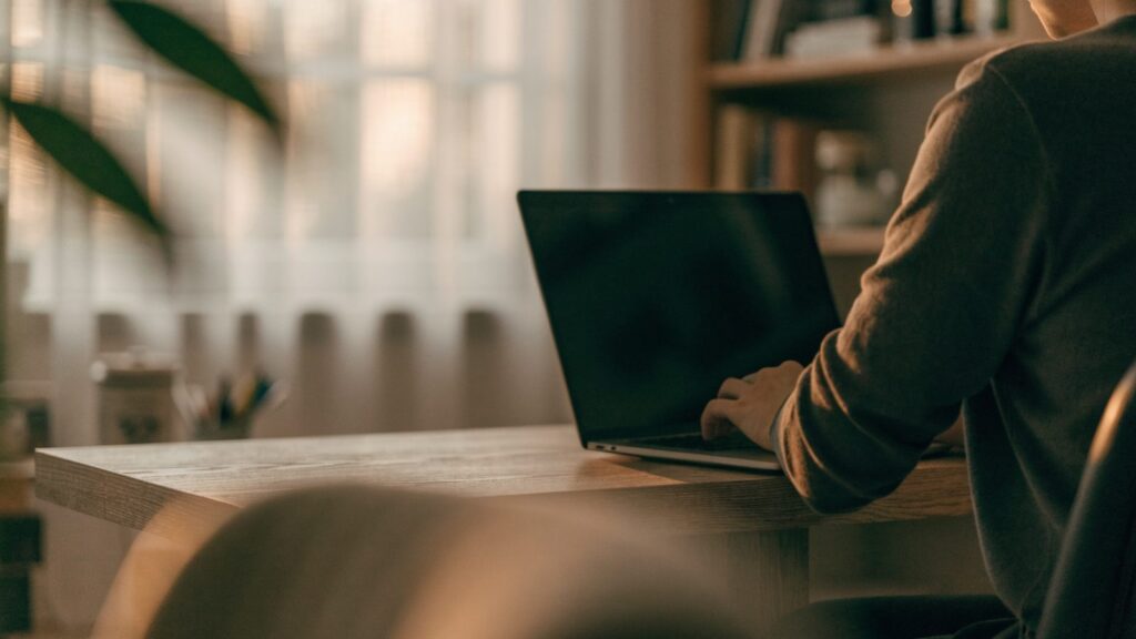 A person seen from behind working on a graphite black laptop in a bright home office