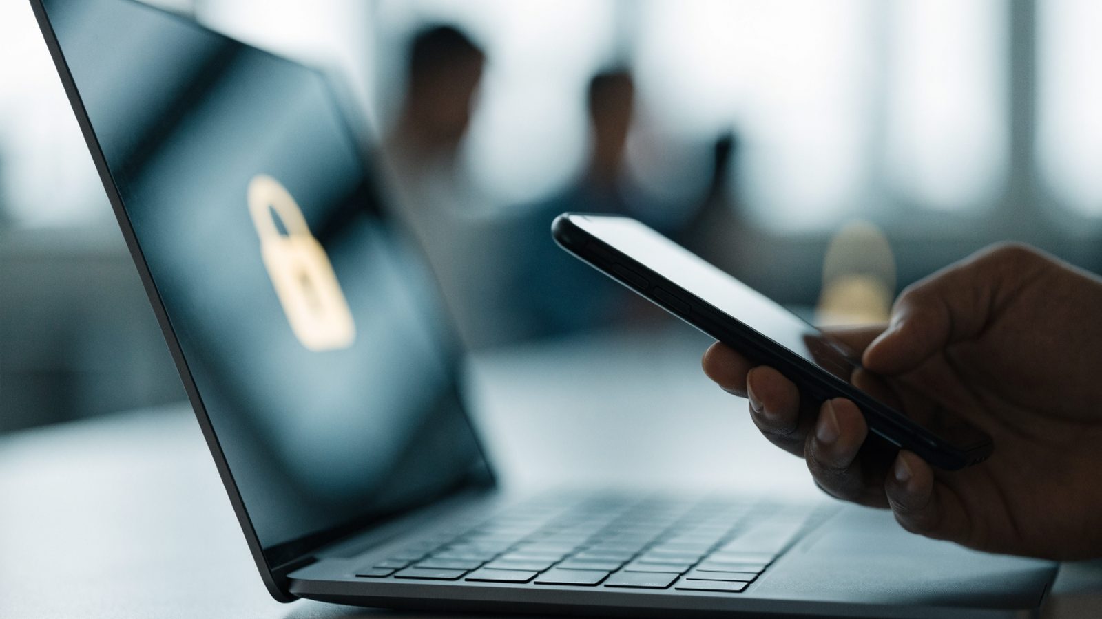 A hand holding a smartphone beside a graphite black laptop