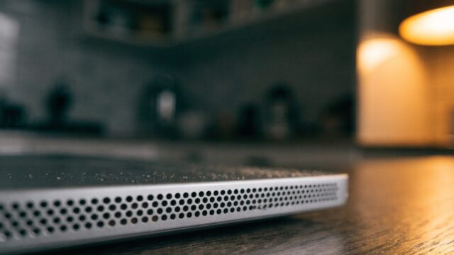 Close-up of the speaker grille edge of a silver laptop on a kitchen table