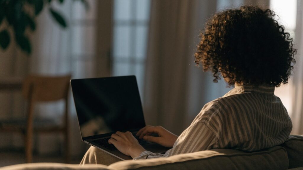 A person seen from behind using a graphite black laptop on a sofa