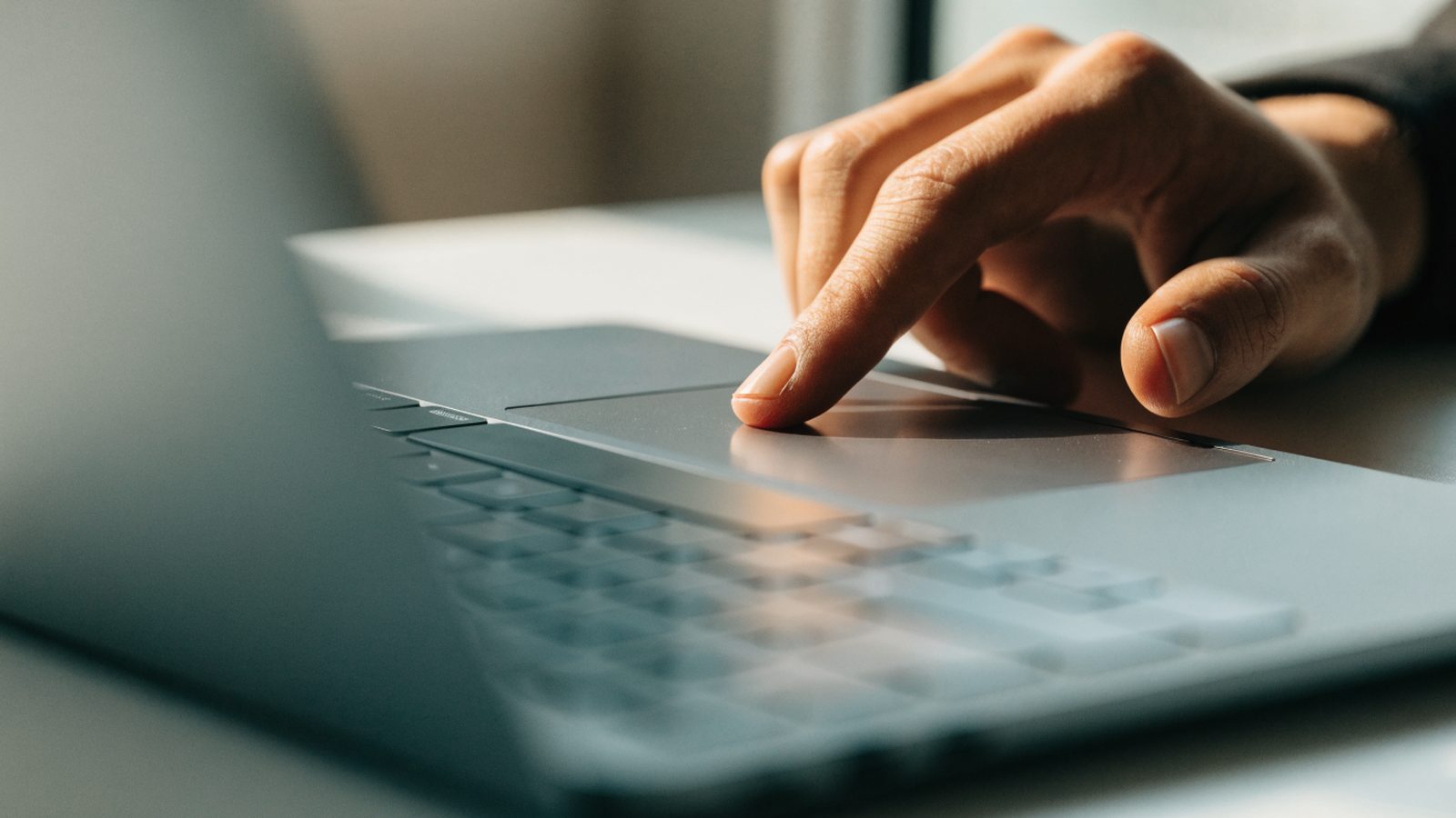 A finger gliding on the touchpad of a matte grey laptop on a white desk