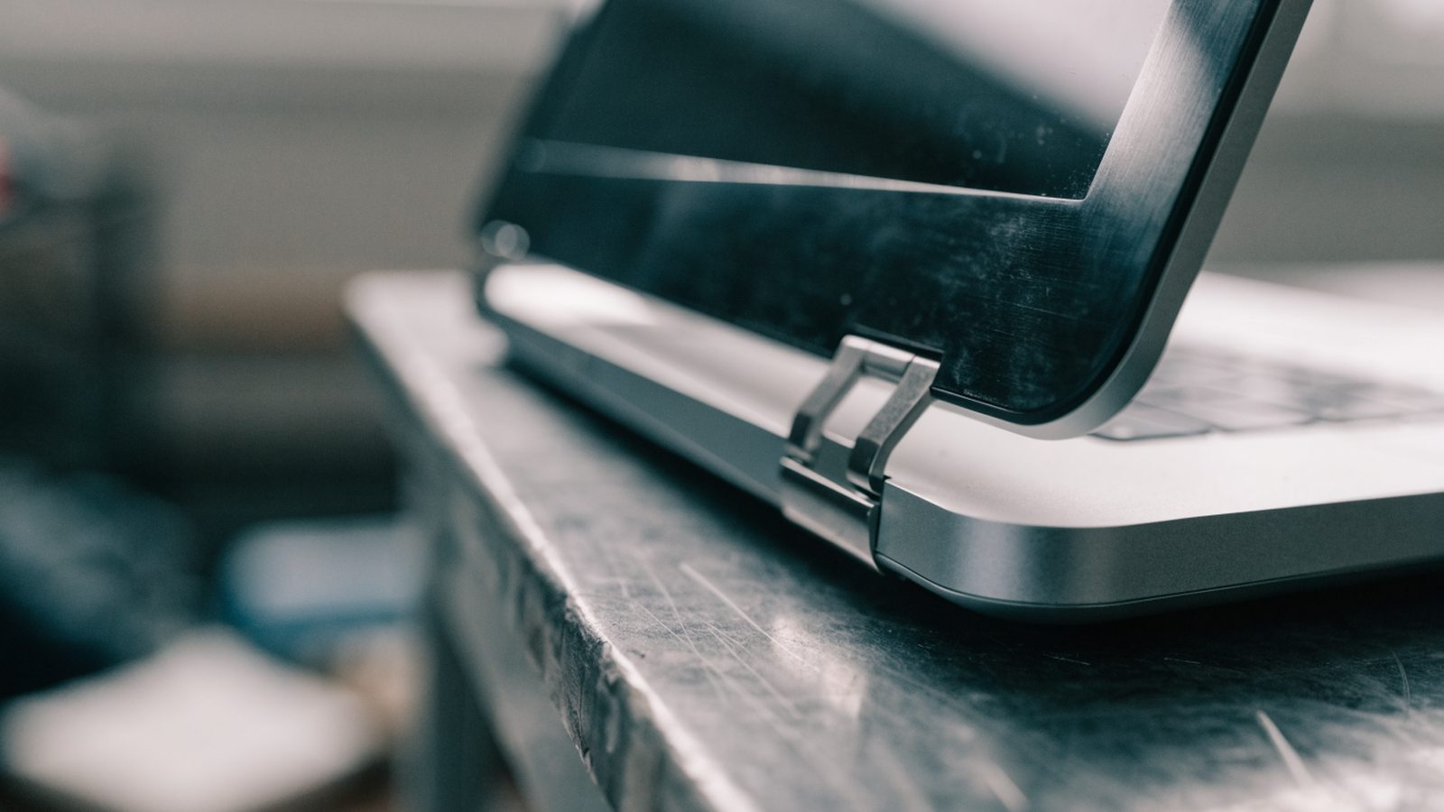 Close-up of the hinge and screen edge of a silver laptop on a workbench