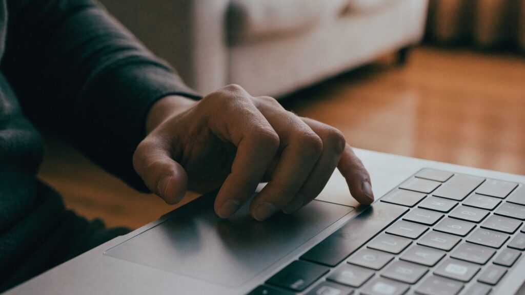 A hand resting on a silver laptop trackpad