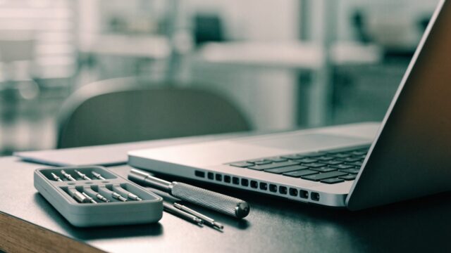 A precision screwdriver kit laid out beside a partially opened silver laptop on an office desk