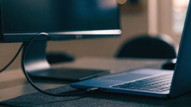 A dark blue laptop connected to a large external monitor with a blank dark screen via a cable on a dark desk m