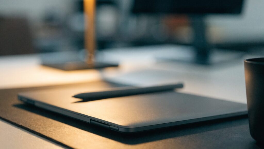 A stylus pen resting on a 2-in-1 matte grey laptop in tablet mode on a dark desk mat