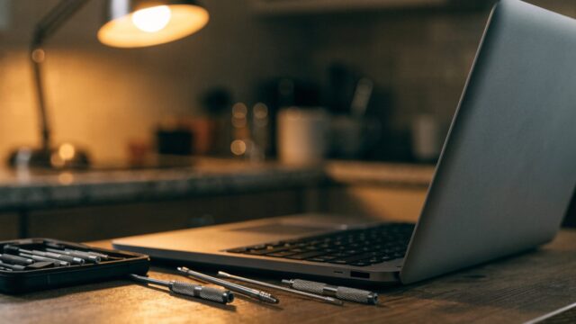 A precision screwdriver kit laid out beside a partially opened matte grey laptop on a kitchen table