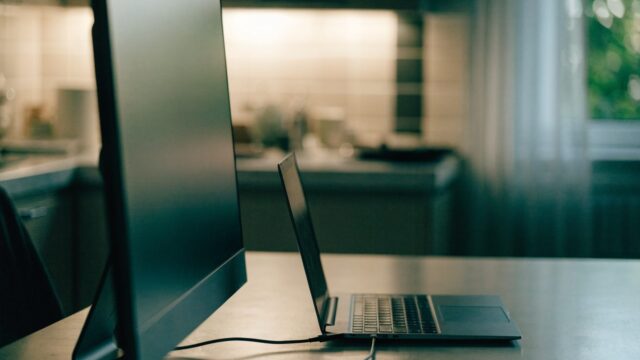 A graphite black laptop connected to a large external monitor with a blank dark screen via a cable on a kitche