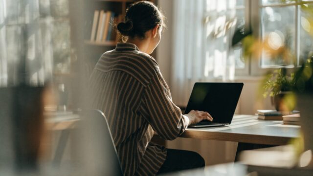 A person seen from behind working on a graphite black laptop in a bright home office