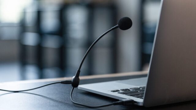 A USB headset with microphone plugged into a silver laptop on a dark desk mat