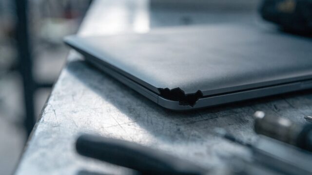 Close-up of a cracked corner on a closed matte grey laptop on a workbench
