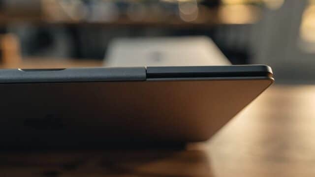 Close-up of the hinge and screen edge of a graphite black laptop on a wooden desk