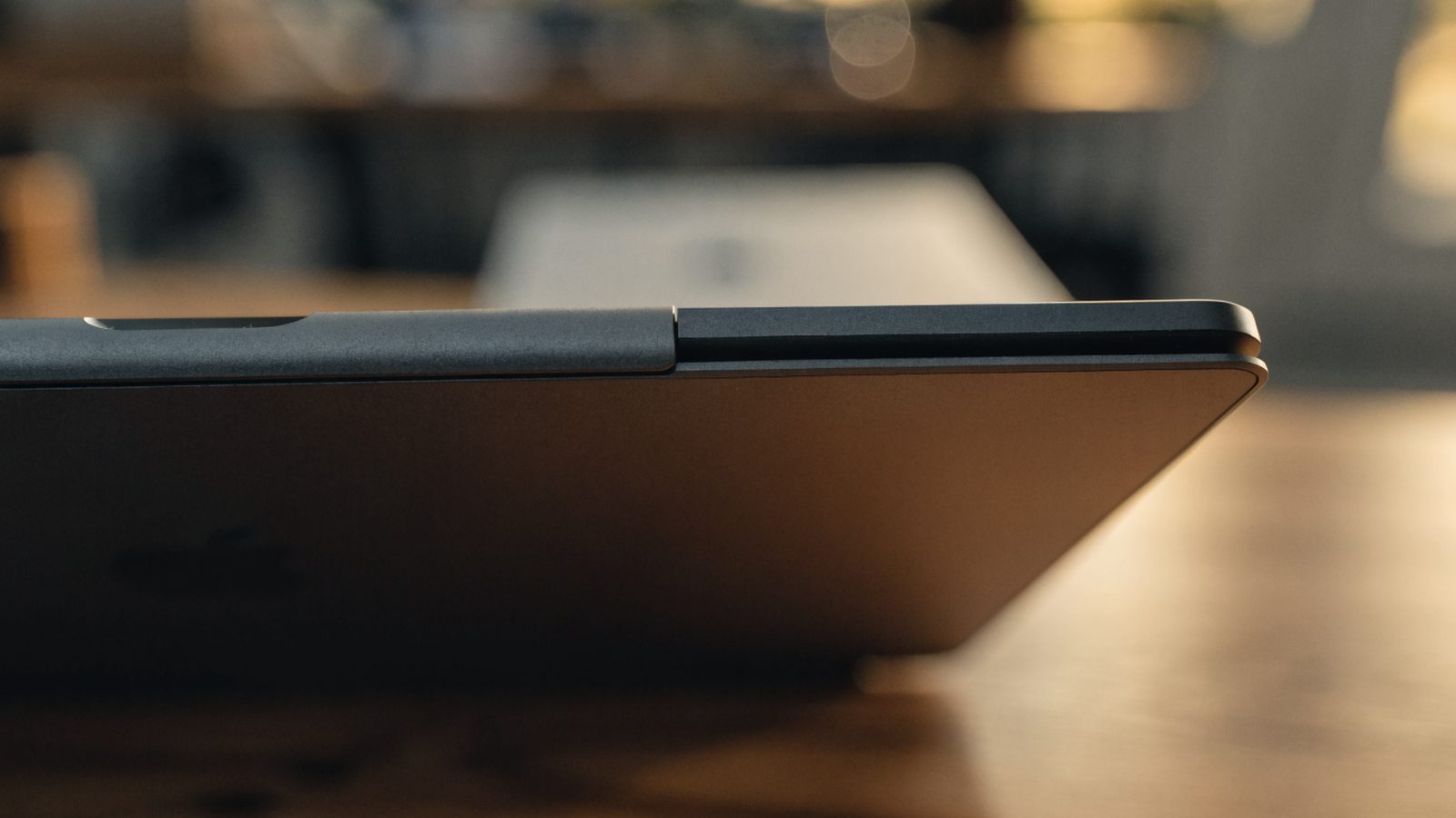 Close-up of the hinge and screen edge of a graphite black laptop on a wooden desk