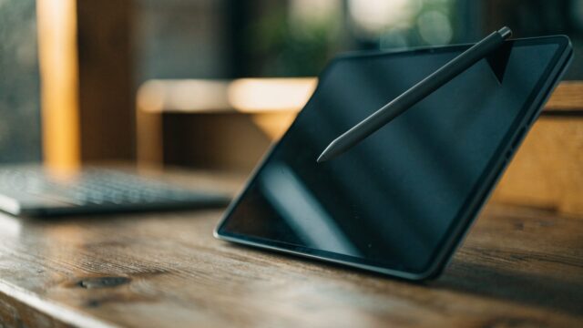 A stylus pen resting on a 2-in-1 graphite black laptop in tablet mode on a wooden desk