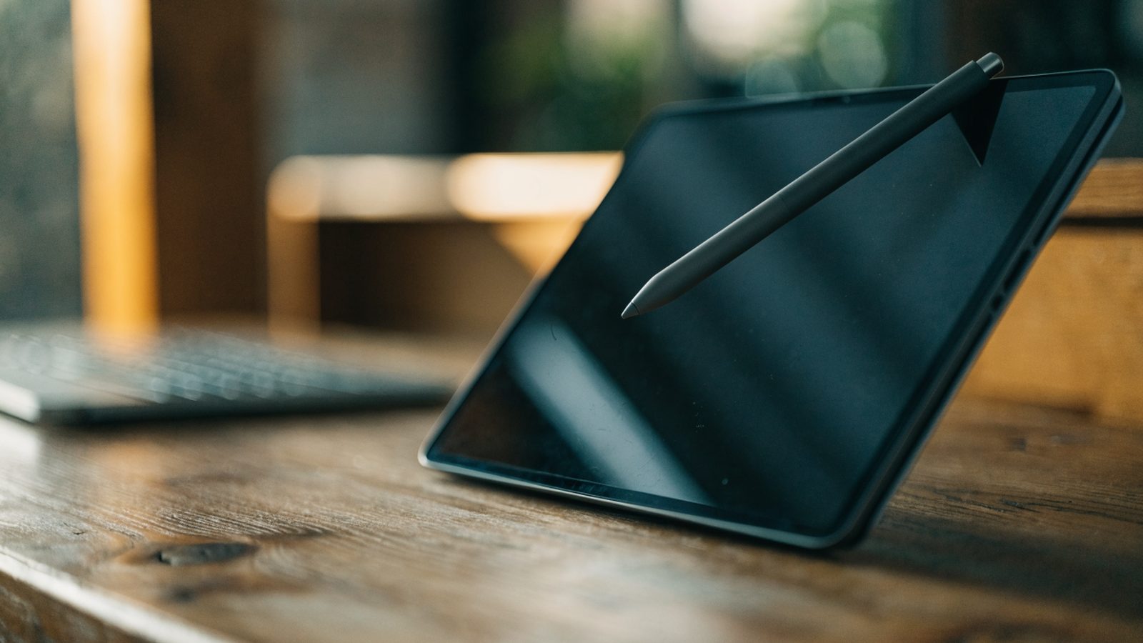 A stylus pen resting on a 2-in-1 graphite black laptop in tablet mode on a wooden desk