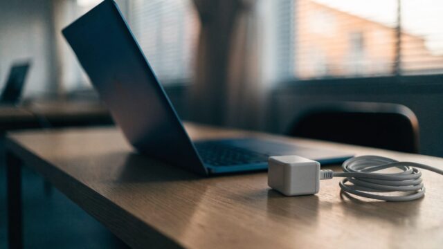 A dark blue laptop on an office desk next to a compact white power adapter with its cable neatly coiled