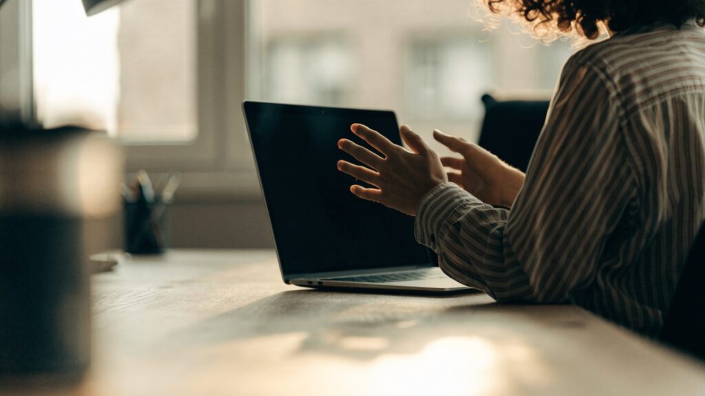 A person seen from behind with hands raised at a graphite black laptop with a dark blank screen on an office d