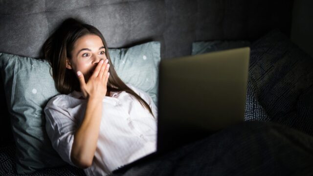 Young woman in bed with laptop in the night