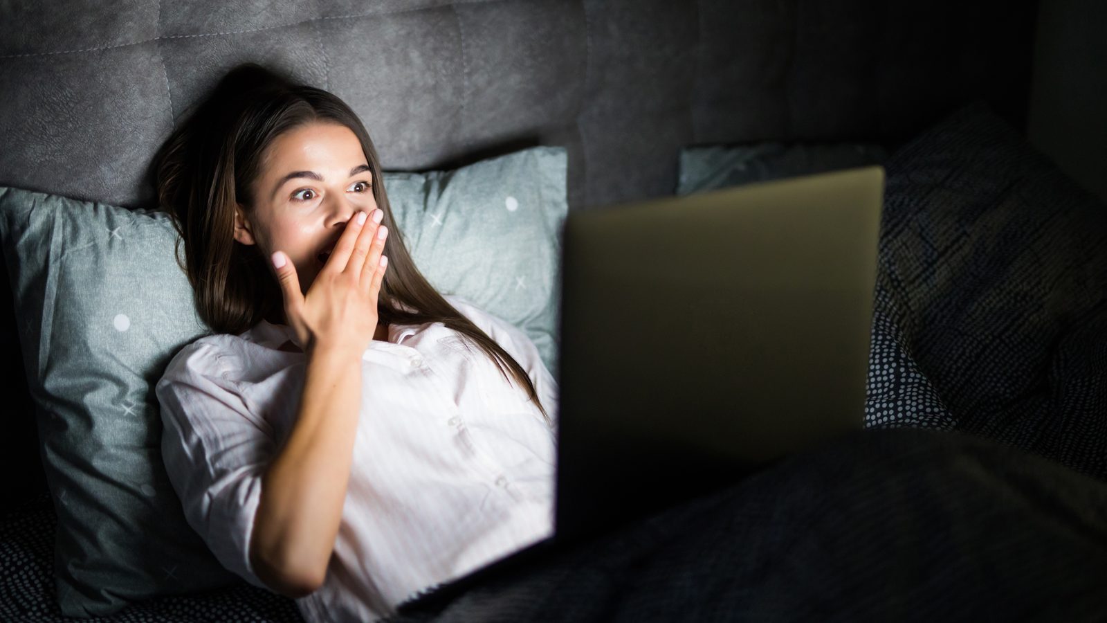 Young woman in bed with laptop in the night