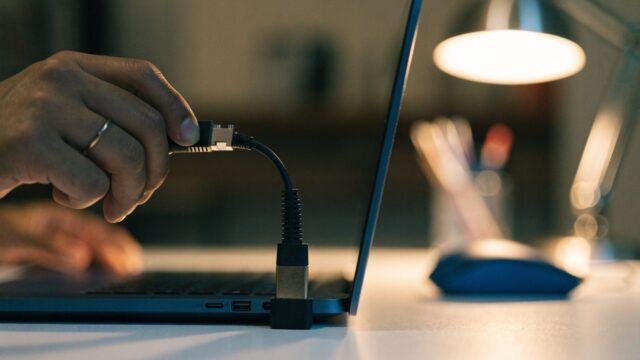 An ethernet cable being plugged into a USB-C adapter connected to a dark blue laptop on a white desk
