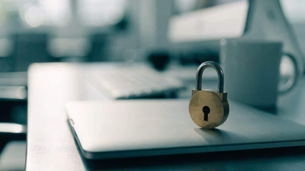 A small brass padlock resting on the closed lid of a silver laptop on an office desk