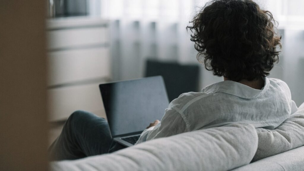 A person seen from behind using a matte grey laptop on a sofa