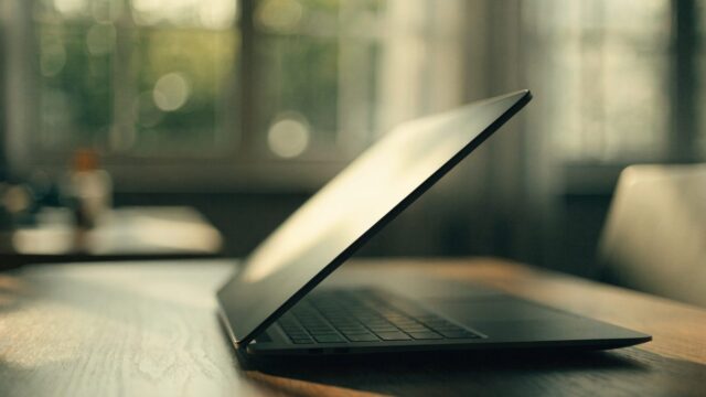 A half-closed graphite black laptop on a wooden desk