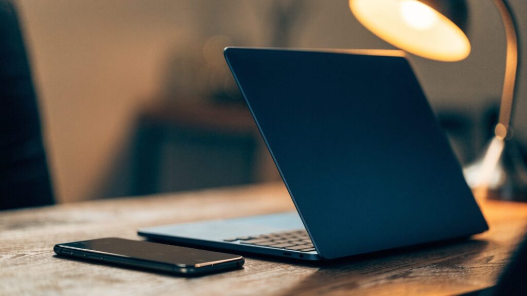 A smartphone lying beside a dark blue laptop on a wooden desk
