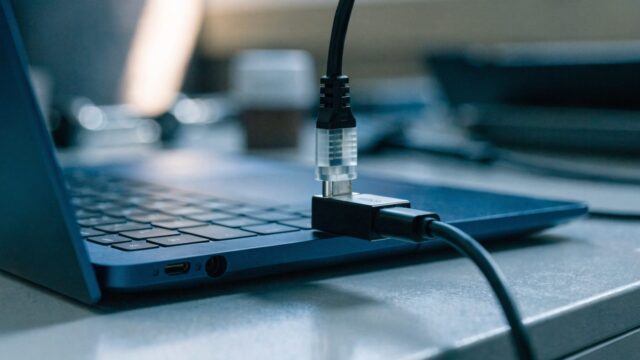 An ethernet cable being plugged into a USB-C adapter connected to a dark blue laptop on a workbench