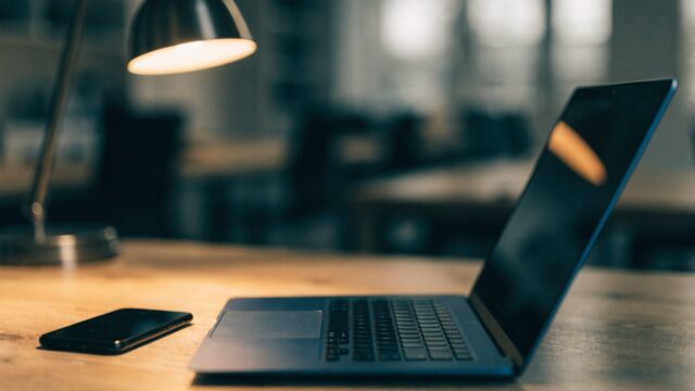 A smartphone lying beside a dark blue laptop on an office desk