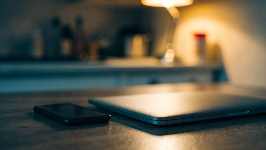 A smartphone lying beside a matte grey laptop on a kitchen table