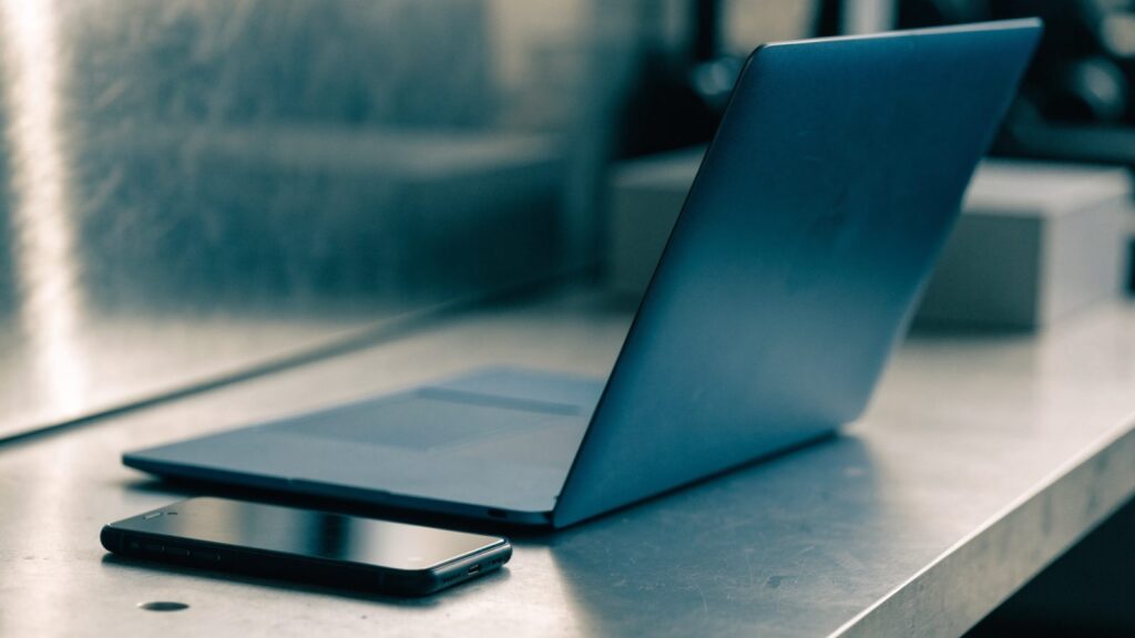 A smartphone lying beside a dark blue laptop on a workbench