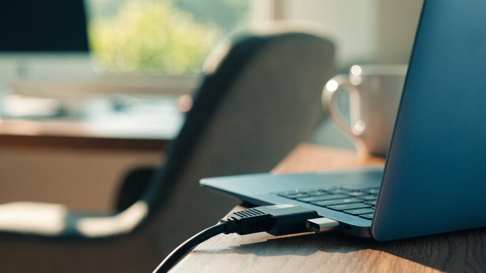 An ethernet cable being plugged into a USB-C adapter connected to a dark blue laptop on an office desk
