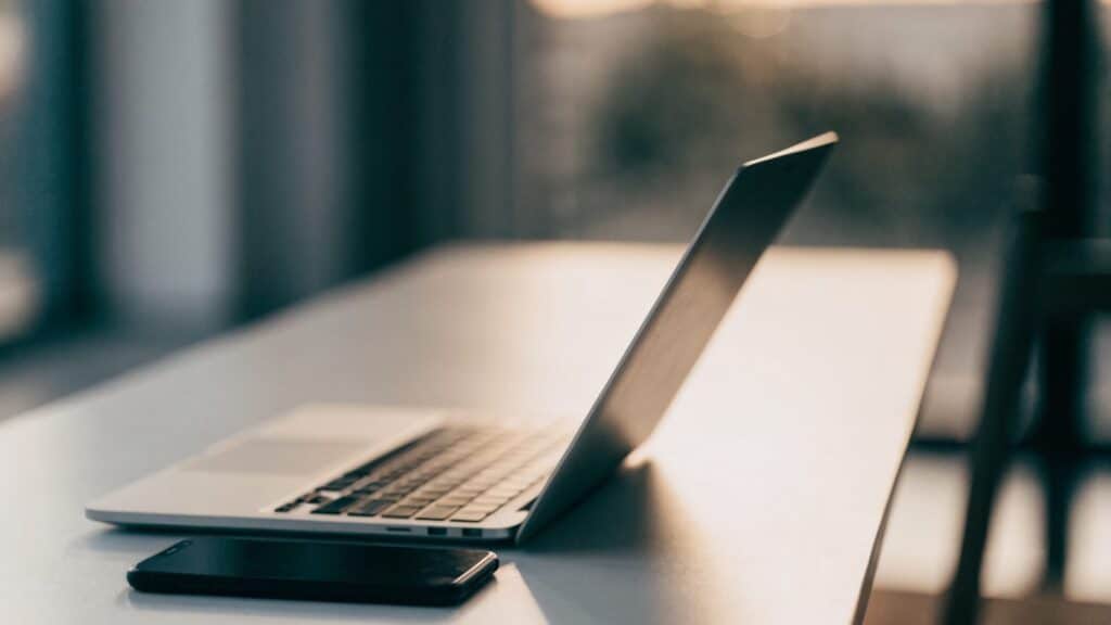 A smartphone lying beside a silver laptop on a white desk