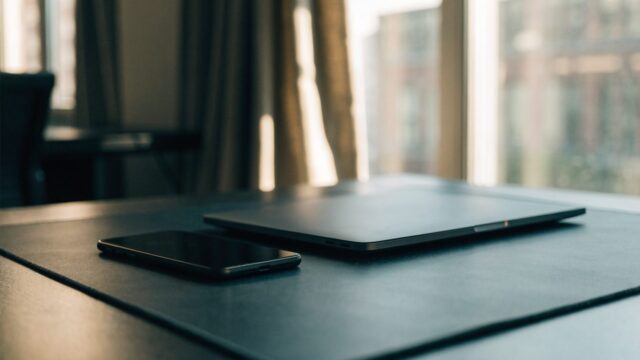 A smartphone lying beside a graphite black laptop on a dark desk mat