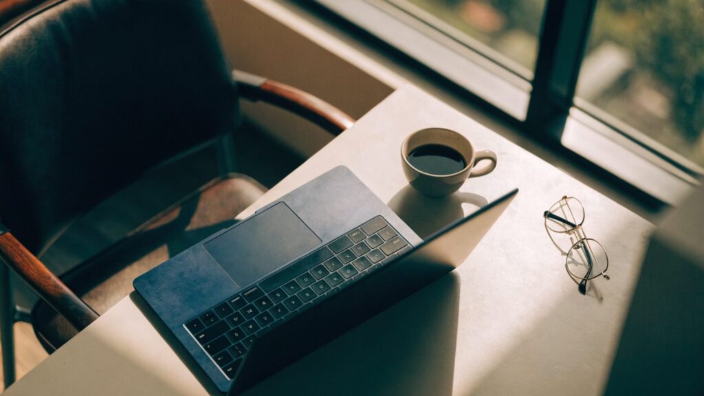 Top-down view of a dark blue laptop on an office desk with a coffee cup and glasses