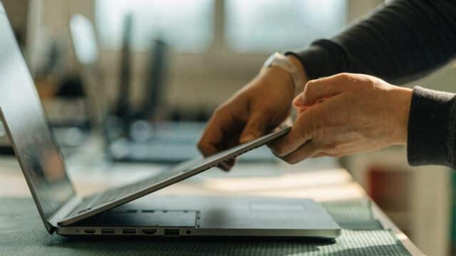 A technician lifting the bottom cover off a matte grey laptop on an anti-static mat