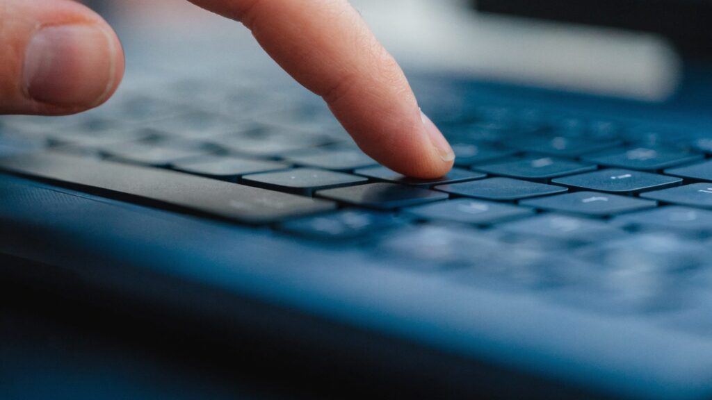 Close-up of a single key being pressed on a dark blue laptop keyboard