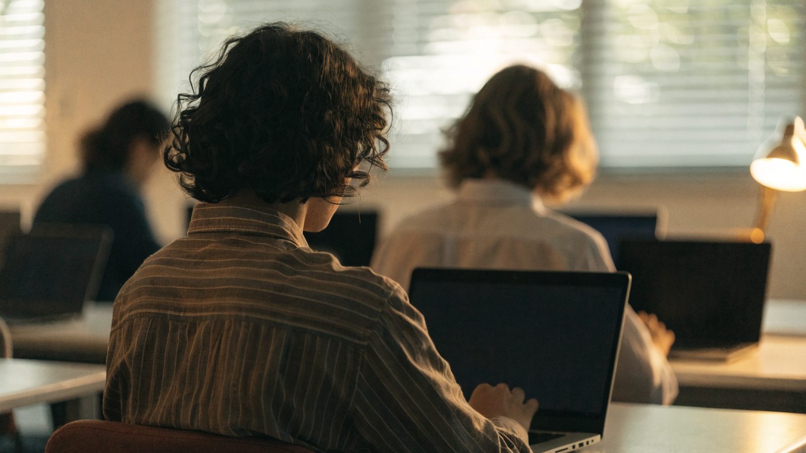 Students seen from behind working on laptops in a bright classroom