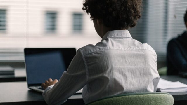 A teenager seen from behind doing homework on a silver laptop at a desk